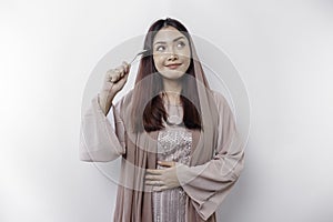 An Asian Muslim woman is fasting and hungry and holding cutlery while looking aside thinking about what to eat