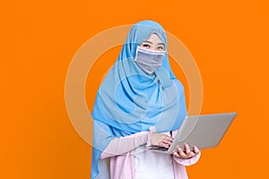 Asian muslim woman in medical mask Coronavirus pandemic disease using laptop computer isolate background. COVID-19 virus epidemic