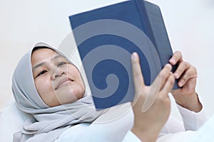 Asian muslim woman reading holy Quran on bed, reciting to memorize Quran before sleep photo