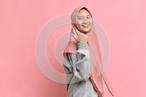 Asian muslim woman smiling and pointing to presenting something on her side with copy space