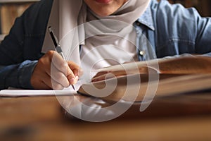 Asian muslim woman studying in library, exam preparation concept. Female college student doing research and making notes in her
