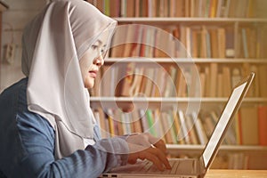 Asian muslim woman studying in library, exam preparation concept. Female college student using laptop to learn online