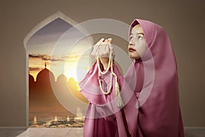 Asian Muslim woman in veil praying with prayer beads on her hands