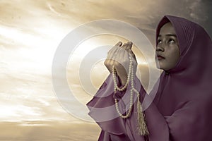 Asian Muslim woman in veil praying with prayer beads on her hands