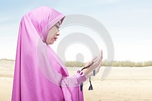 Asian Muslim woman in veil praying with prayer beads on her hands