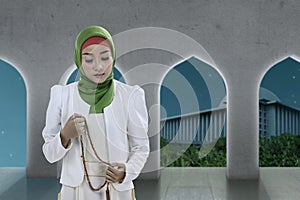 Asian Muslim woman in veil praying with prayer beads on her hands