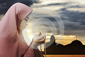 Asian Muslim woman in veil praying with prayer beads on her hands