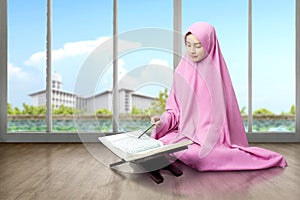 Asian Muslim woman in a veil sitting and reading the Quran