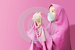 Asian Muslim woman in a veil and wearing flu mask praying with prayer beads