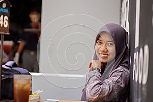 Asian Muslim woman wearing modern hijab sitting and leaning against in cafe wall