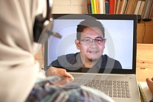 Asian muslim woman having video teleconference witha man on her laptop at home, online learning or working from home photo