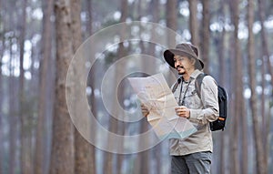 Asian naturalist looking at the map for direction while exploring wildlife in the pine forest for surveying and discovering the