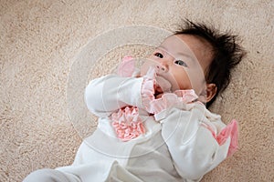 Asian newborn baby girl 3 months old is lying on the bed with her hands clasped and releasing and covering her face happily while