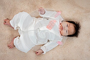 Asian newborn baby girl 3 months old is lying on the bed with her hands clasped and releasing and covering her face happily while