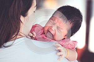 Asian newborn baby girl crying with tried on mother`s shoulder
