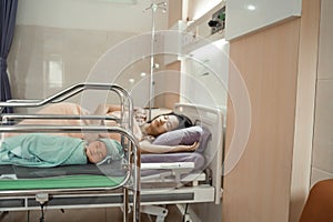 Asian newborn baby laying in crib with his mother lying on bed side