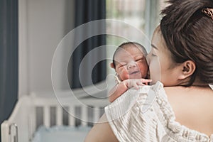 Asian newborn baby with mother on the bed. Mom holding and kissing her child