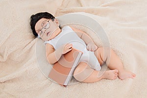 Asian newborn baby wear glasses deeply sleeping and napping with favorite book on beige blanket with safe and comfortable.