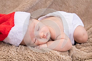 Asian newborn baby wearing christmas hat sleeping on brown blanket, adorable infant lying on bed at home with trust and safe.