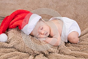 Asian newborn baby wearing christmas hat sleeping on brown blanket, adorable infant lying on bed at home with trust and safe.