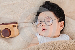 Asian Newborn baby wearing glasses sleeping with beige blanket next to toy camera with safe and comfortable. Adorable baby resting