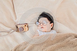 Asian Newborn baby wearing glasses sleeping with beige blanket next to toy camera with safe and comfortable. Adorable baby resting