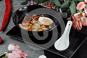 Asian noodle soup, ramen with chicken, tofu, vegetables and egg in black bowl. Slate background