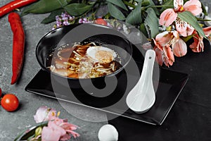 Asian noodle soup, ramen with chicken, tofu, vegetables and egg in black bowl. Slate background