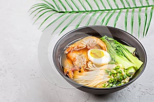 Asian noodle soup, ramen with prawn shrimp, vegetables and egg in black bowl on gray concrete background. Flat lay, Top view, mock