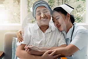 Asian nurse gentlely hug senior cancer patient who wearing headscraf after chemotherapy to encourage patein to fight with sickness