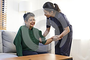 Asian nurse help old lady stand up from a couch.