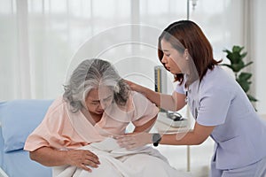 Asian nurse helping a senior Asian female patient with stomach ache on a bed in hospital