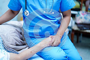 Asian nurse physiotherapist doctor care, help and support senior or elderly old lady woman patient lie down in bed at hospital war