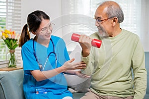 Asian nurse physiotherapist helping senior man in lifting dumbell at retirement home