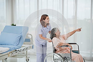 Asian nurse pushing senior female patient in a wheelchair at the hospital ward