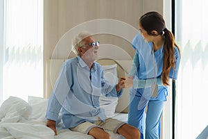 Asian nurse standing on a home bed next to an older man helping hands, care. Elderly patient care and health lifestyle, medical