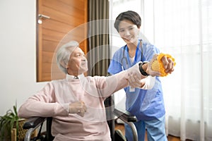 Asian nurse taking care of an elderly man sitting on wheelchair , doing hand exercises at  senior healthcare center