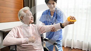 Asian nurse taking care of an elderly man sitting on wheelchair , doing hand exercises at  senior healthcare center