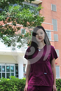 Asian Nurse Wearing Scrubs Stands in Front of Hospital