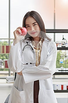 Asian nutritionist doctor woman showing red apple in right hand in laboratory room