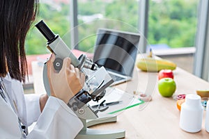 Asian nutritionist doctor woman working microscope and labtop on wooden table