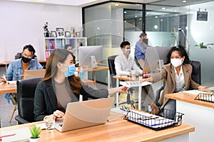 Asian office workers wearing face masks working in new normal office and doing social distancing