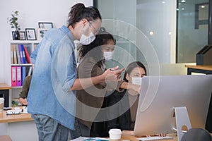 Asian office workers wearing face masks working in new normal office and doing social distancing