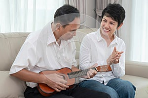 Asian okd couple sing a song and play ukulele togather in living