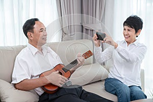 Asian old couple sing a song and play ukulele togather in living