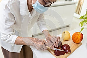 Asian old elderly people in a medical face mask,cutting the rose apple into slices,senior woman eating fresh fruit or nutritious