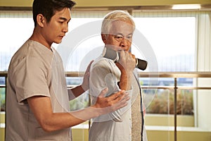 Asian old man exercising using dumbbell in rehab center