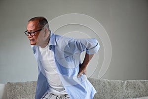 Asian old man sitting on sofa and having a back pain, backache at home. Senior healthcare concept