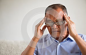Asian old man sitting on sofa and having a headache at home. Senior healthcare concept