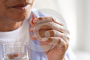Asian old man taking in pill and another hand holding a glass of clean mineral water. Senior healthcare and medicine concept